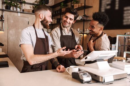 129503056-three-cheerful-men-baristas-standing-behind-the-counter-at-the-coffee-shop-using-mobile-phone